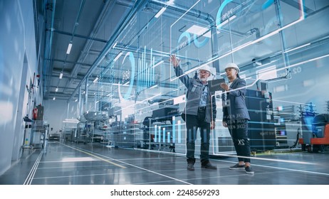 Factory Digitalization: Two Industrial Engineers Use Tablet Computer, Visualize the Wall of Big Data Statistics, Optimization of High-Tech Electronics Facility. Industry 4.0 Machinery Production Stockfoto