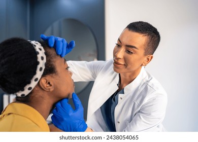 Facial aesthetics surgery consultations at medical beauty clinic. Young woman professional aesthetician examining patient's face, touching it with gloved hands. Stockfotó