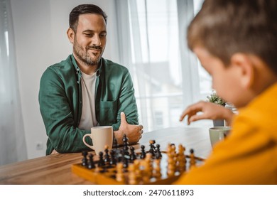Стоковая фотография: Father with cup of hot drink and son caucasian play chess together at home