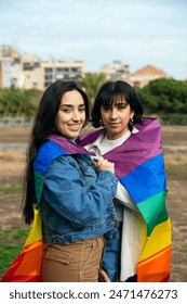 Female couple wrapped in a rainbow pride flag smiling directly at the camera,symbolizing lgbtq friendship and acceptance. Arkistovalokuva