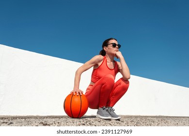 Female basketball player, crouching holding a basketball, outside in the sun. Foto stock