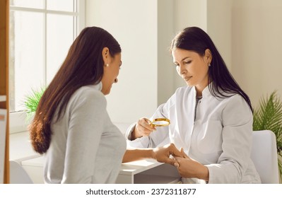 Female dermatologist examining skin of woman patient with magnifying glass. General practitioner doing skin examination in dermatology clinic. Professional doctor checking benign moles on arm Stockfotó