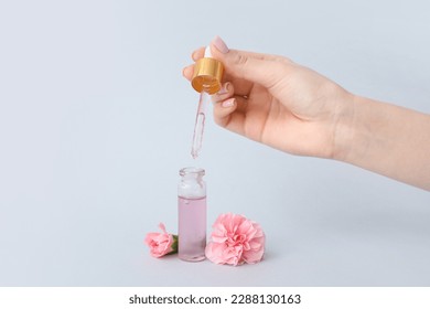 Female hand with bottle of cuticle oil and carnation flowers on light background Foto stock