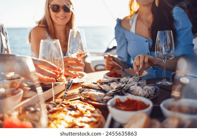 船上でお祝いの宴会。おいしい食べ物とテーブルの接写。若い笑顔の女性はワインやカクテルのメガネでトーストを上げます。ボート上の楽しいbacheloretteパーティー。クルーズ中のランチ。の写真素材