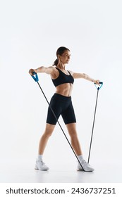 Fit young woman in black sportswear training, using resistance bands for arm exercise isolated over white studio background. Concept of sport, health and body care, fitness app, exercises templates Arkistovalokuva