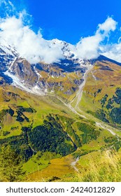  Flowering alpine meadows and mountains of the Hohe Tauern Park. The famous mountain road Grossglognerstrasse. Austria. Snowy mountain peaks covered with clouds. – Ảnh có sẵn