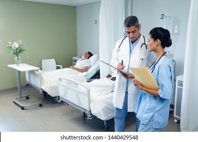 Front view of diverse male and female doctors discussing over clipboard while diverse men sleeping in the ward at hospital Stockfoto