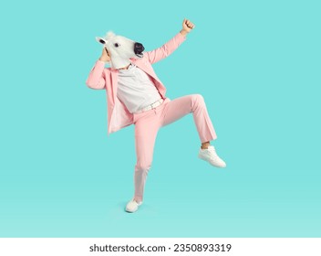 Funny crazy man wearing horse head mask dancing. Full length shot of eccentric creative guy in pastel pink suit dancing and having fun over isolated on light blue studio background 库存照片