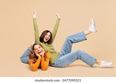 Full body happy young friends two women wear orange green shirt casual clothes together sit lay down raise up leg hands do winner gesture isolated on plain pastel beige background. Lifestyle concept Foto de stock