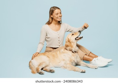 Full body side view young smiling happy owner woman she wear casual clothes sits give her best friend retriever dog treats isolated on plain light blue background studio. Take care about pet concept 库存照片