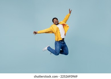 Full body young fun man of African American ethnicity 20s wear yellow shirt jump high with outstretched hands isolated on plain pastel light blue background studio portrait. People lifestyle concept Foto stock