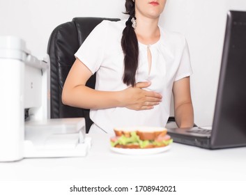 Girl office worker near which lies a sandwich holding on to a stomach in which there is pain and inflammation in the stomach. Concept of indigestion and malnutrition in office workers, gastritis and Arkistovalokuva