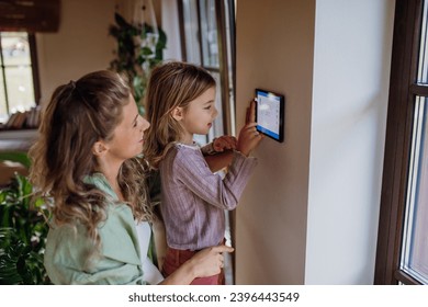 女の子は母親が調整するのを助け、サーモスタットの加熱温度を下げます。家庭用暖房およびサーモスタットにおける持続可能で効率的でスマートな技術の概念。の写真素材