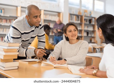 Group of young adult multiracial people studying in library, talking, reading books and writing in notepads Stock-foto