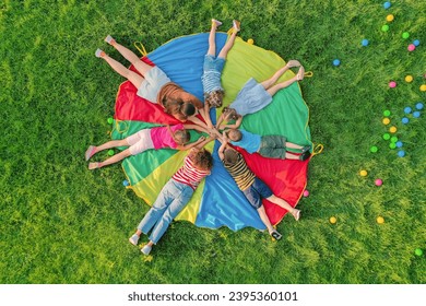 Groupe d'enfants avec des enseignants tenant la main ensemble sur l'aire de jeux de l'arc-en-ciel parachute dans le parc, vue de dessus. Activités du camp d'été : photo de stock