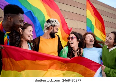 Group of excited young friends enjoying together on gay pride day. Joyful people gathered from LGBT community hugging laughing outdoors. Generation z and open minded.  Foto Stock