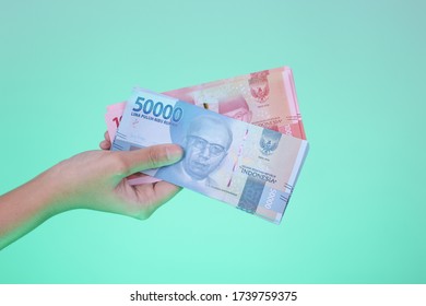 シアンの背景にインドネシアの通貨を持つ手、10万枚と5万枚のルピアの紙幣の写真素材