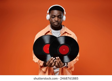 Handsome African American man in stylish attire holding a record and listening with headphones. Arkistovalokuva