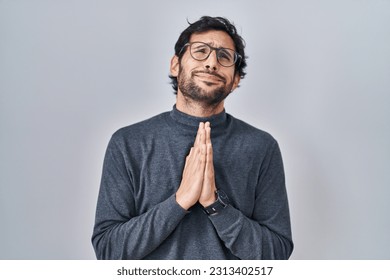 Handsome latin man standing over isolated background begging and praying with hands together with hope expression on face very emotional and worried. begging. : stockfoto