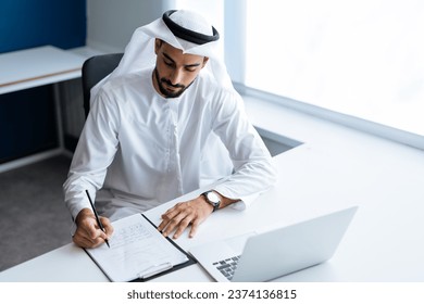handsome man with dish dasha working in his business office of Dubai. Portraits of a successful businessman in traditional emirates white dress. Concept about middle eastern cultures. Arkistovalokuva