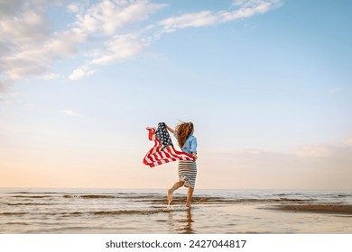 Happy woman holding United States of America flag and running  on the beach at sunset. Patriotic holiday. USA celebrate 4th of July. Independence Day concept Foto stock
