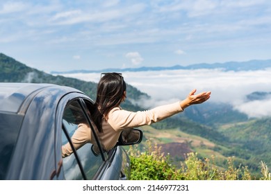 Happy young Asian woman enjoying sitting in a car watching a beautiful mountain view, hand greeting. Driving road trip on vacation and adventure concept: stockfoto