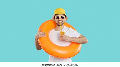 Happy young man with inflatable swimming circle and with glass of juice enjoys summer vacation. Cheerful funny guy in summer clothes drinks juice on light blue background. Summer relaxation concept. Stock Photo