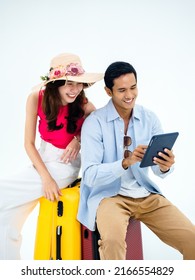 Happy Asian couple, young woman with beach hat and man in denim shirt sit on suitcase, using tablet together for trip information isolated on white background, ready to travel, happy summer holiday. Arkivfotografi