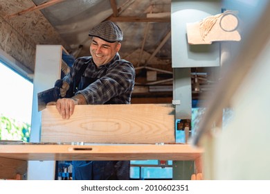 作業場で作業台で板材を切りながら鋭いのこぎりを使う幸せな大工の写真素材