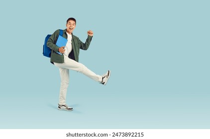 Happy cheerful university, college or high school student boy in casual clothes with backpack and notebook walking in funny way on light blue blank copy space studio background – Ảnh có sẵn