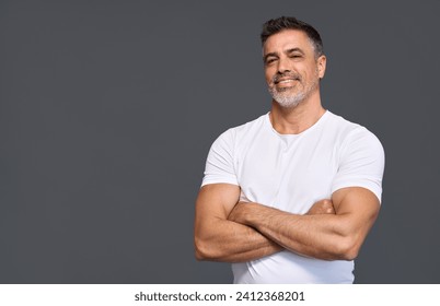 Happy fit sporty older man coach, middle aged sportsman athlete or personal trainer wearing white t-shirt showing muscles standing isolated on gray background advertising gym membership. Portrait. 库存照片
