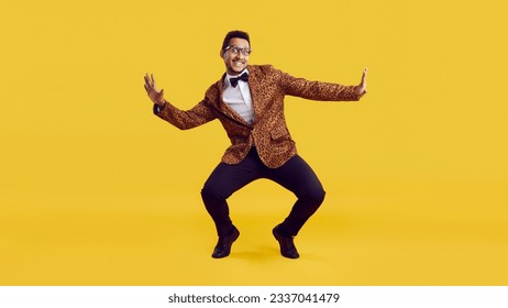 Happy funny young man dancing isolated on yellow colour background. Full body shot of handsome positive goofy confident ethnic guy in leopard party jacket with bowtie dancing and having fun in studio 库存照片