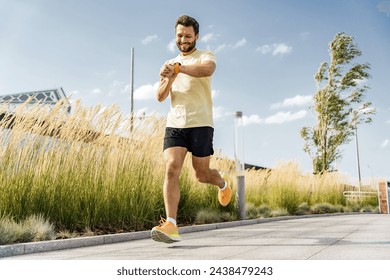 Happy man checking progress on fitness watch while running, tall grass background, sunny day.

 Foto stock