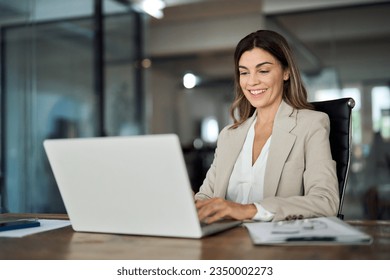 Happy mature business woman entrepreneur in office using laptop at work, smiling professional middle aged 40 years old female company executive wearing suit working on computer at workplace. Foto stock