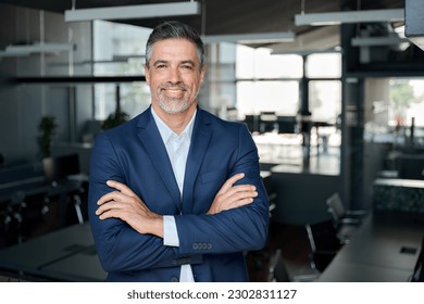 Happy middle aged business man ceo standing in office arms crossed. Smiling mature confident professional executive manager, proud lawyer, confident businessman leader wearing blue suit, portrait. స్టాక్ ఫోటో
