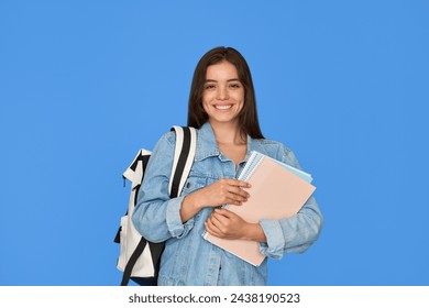 Feliz guapa gen una chica latina sonriente estudiante sosteniendo mochila y cuadernos usando chaqueta de mezclilla mirando a la cámara de pie aislado en el fondo azul de la educación publicitaria curso. Retrato. Foto de stock