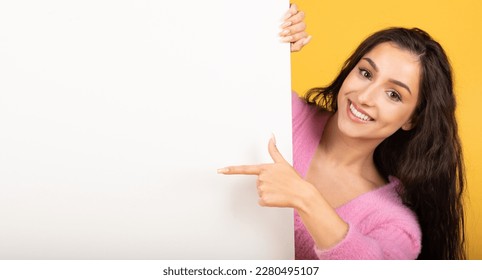 Happy pretty young caucasian brunette woman point finger at banner with blank space for words, isolated on yellow studio background. Great ad and offer, huge sale, recomendation Foto stock