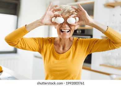 계란으로 눈을 가리고 부엌에서 즐거운 시간을 보내는 행복한 노년여성  스톡 사진