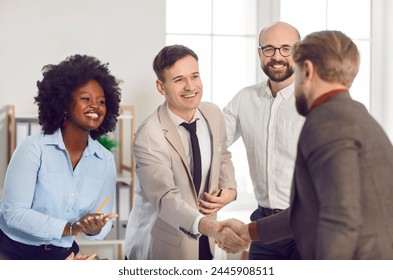 Happy smiling diverse company employees making deal in modern office shaking hands. Business people rejoicing at a successful partnership of colleagues applauding them on a meeting.: stockfoto