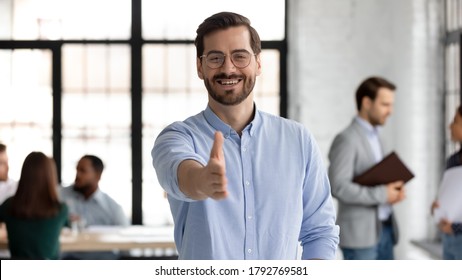 Head shot portrait smiling businessman wearing glasses extending hand for handshake at camera, friendly hr manager greeting candidate on interview, offering deal, welcoming client at meeting