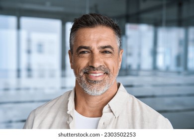 Headshot close up portrait of indian or latin confident mature good looking middle age leader, ceo male businessman on blur office background. Handsome hispanic senior business man smiling at camera. Stockfoto