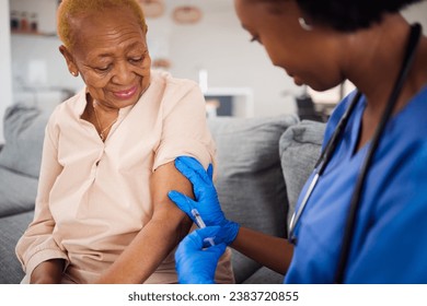 Healthcare, black woman and doctor for a home vaccine, virus safety and security from covid. Smile, medicine and and African nurse with a senior patient and giving a vaccination during a consultation Foto stock