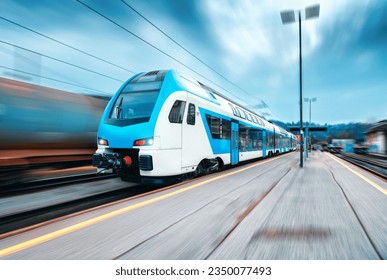 High speed train in motion on the railway station at sunset. Blue modern intercity passenger train with motion blur effect on the railway platform. Railroad in Europe. Commercial transportation - Φωτογραφία στοκ