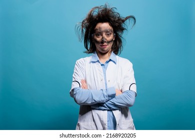 カメラを見て青い背景に立って厄介な髪型と汚い顔と陽気な探してクレイジー化学者。不安定な髪と汚れた顔を持つユーモラスなマッドサイエンティストは、腕を組んで立っている。の写真素材