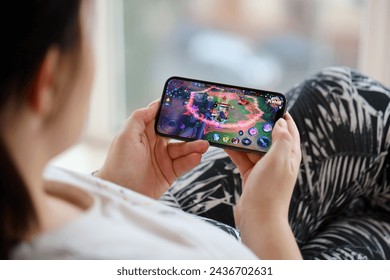 モバイルゲームプレイ中の女性の手の中にiPhone 15スマートフォンの画面でキングスモバイルiOSゲームの名誉。ポータブル デバイスでのモバイル ゲームおよびエンターテイメントのエディトリアル写真素材