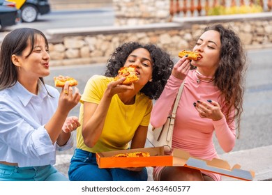 Hungry female multiracial friends eating take away pizza sitting outdoors in the city Stock-foto