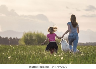 Idyllic scene of mother, daughter and pet dog happily running in the grass field full of dragonflies. Meaning of life concept. Arkistovalokuva