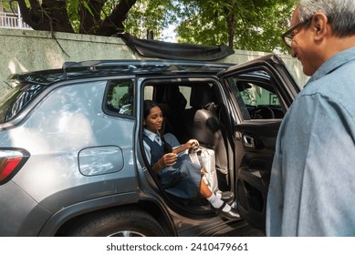 인도 할아버지가 10대 이전 손녀인 손녀가 자신의 가방을 들고 인도 뭄바이에서 방과 후에 차에서 내리는 것을 보고 웃는다. 스톡 사진