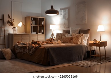 Interior of bedroom with checkered plaid on bed and glowing lamps late in evening Stock Photo