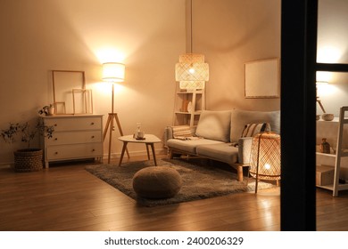 グレイのソファ、コーヒーテーブル、夕方には輝くランプを備えたモダンなリビングルームのインテリアの写真素材